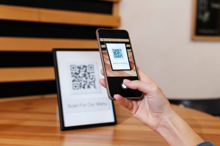 Henkilö skannaa QR-koodia älypuhelimella kyberturvallisuusympäristössä.
